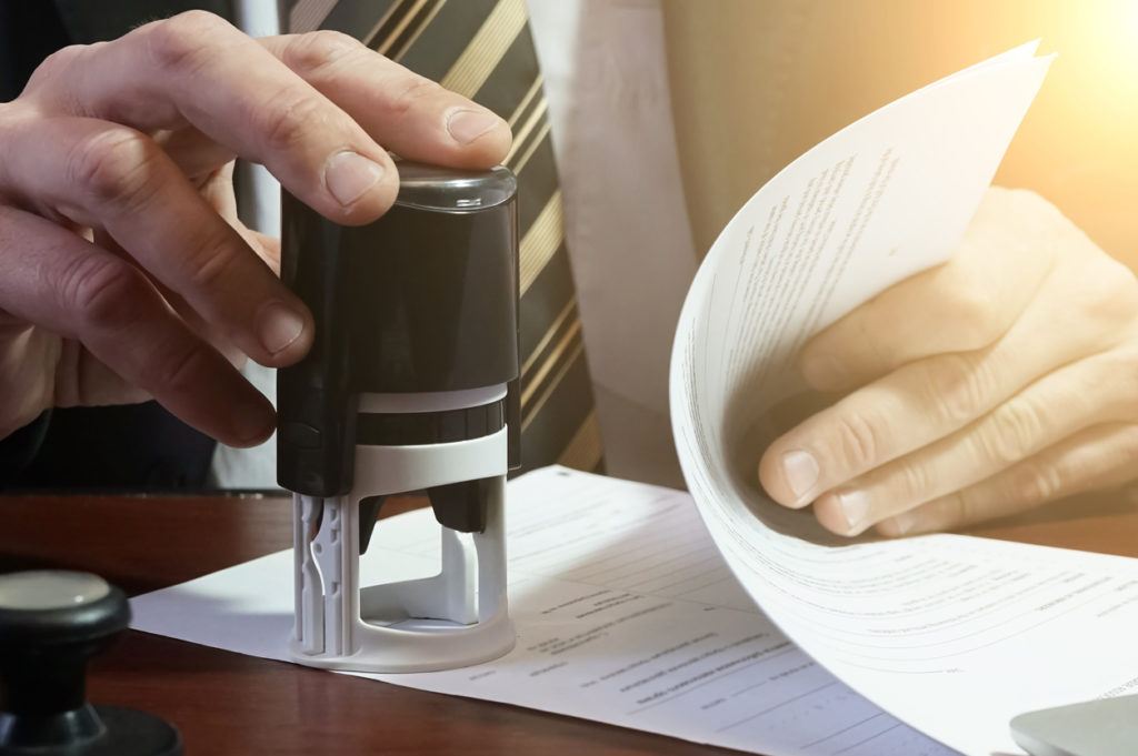 Image of a person stamping a stack of papers at a table.