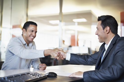 Image of two men shaking hands at a table. 