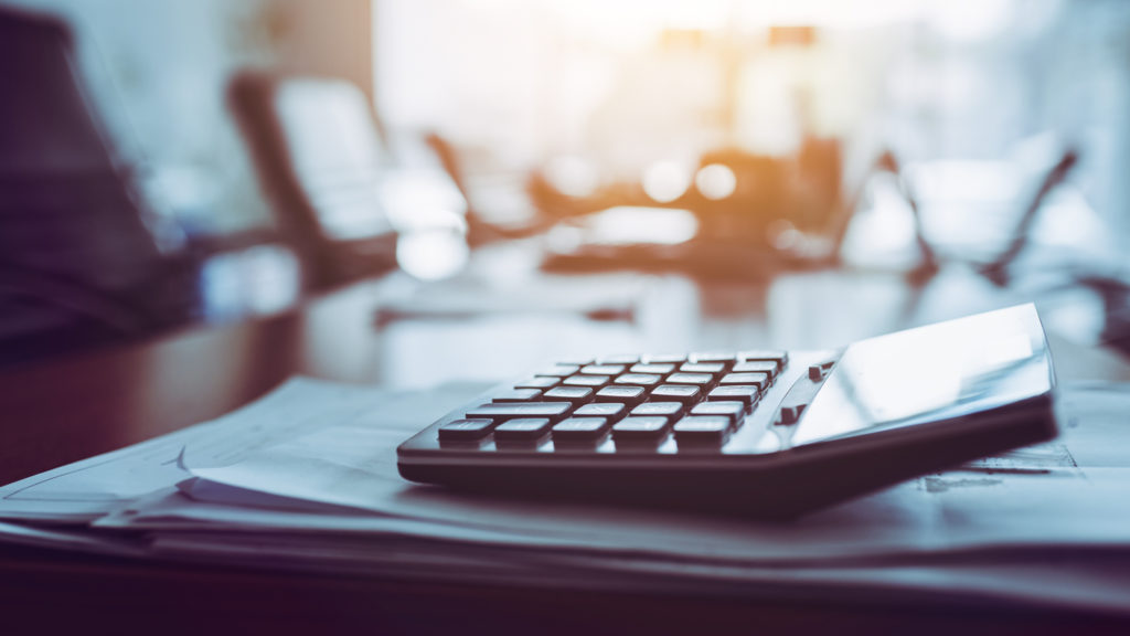 Image with a close up shot of a calculator on business working desk, dark background.