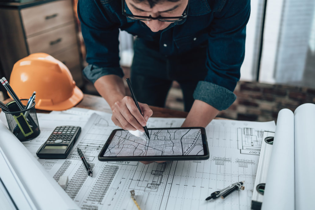 Image of an engineer working with drawings inspection on tablet in the office and Calculator, triangle ruler, safety glasses, compass, vernier caliper on Blueprint. Engineer, Architect, Industry and factory concept.