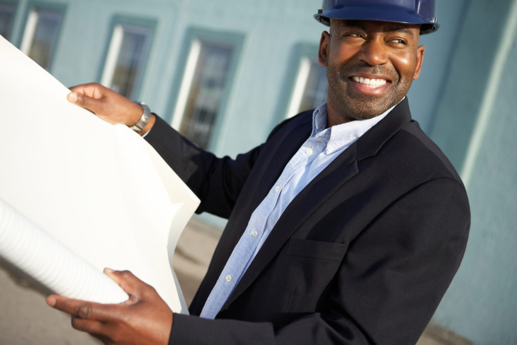 Image of a Businessman in hardhat unrolling paper outdoors.