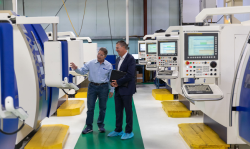Image of two men in a CNC machine shop between a row of automated CNC Machines.