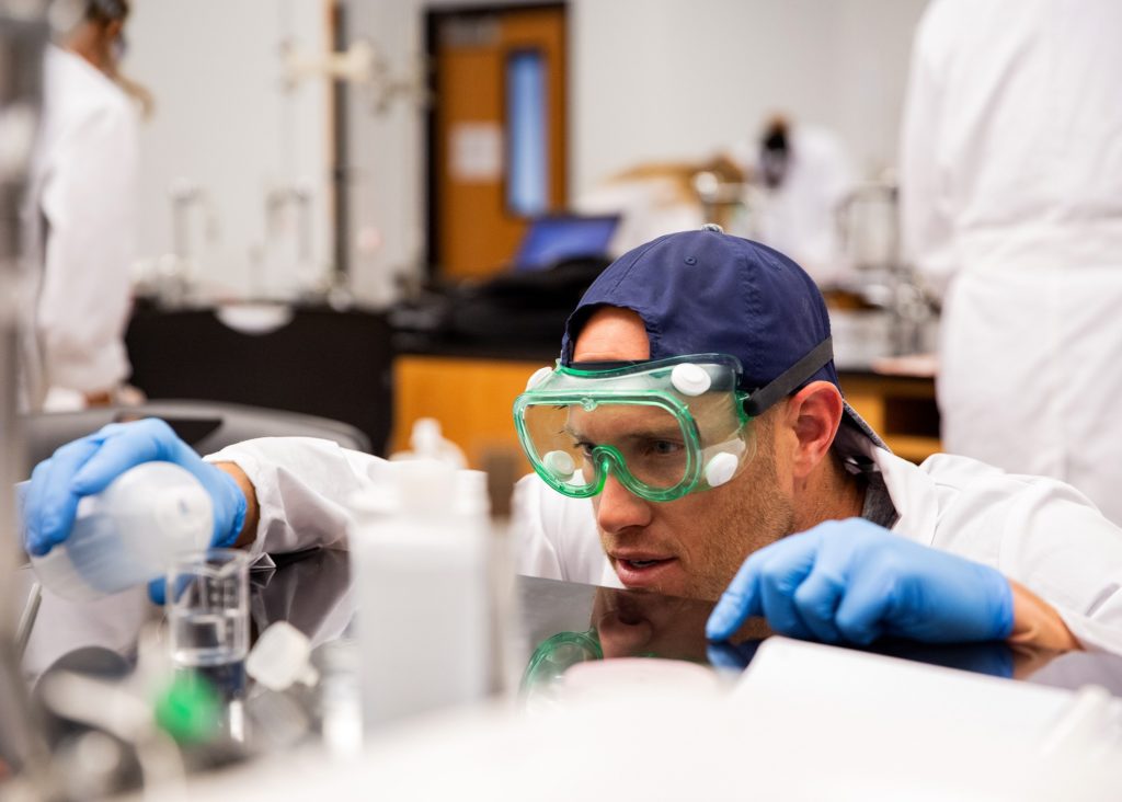 Image of a student in a laboratory pouring fluid into a beaker.