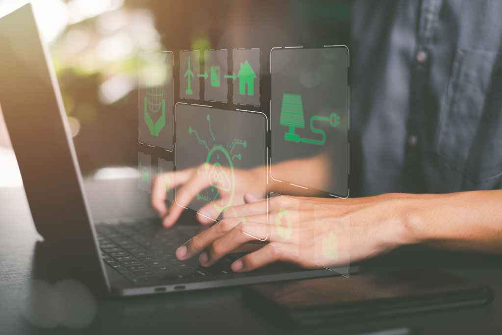 Hands typing on laptop on table with green images hovering over