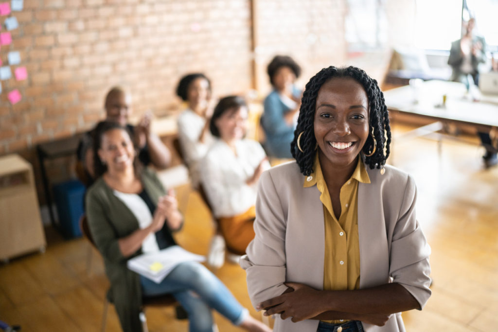 Image of a business woman and a group of women, seated, behind her.