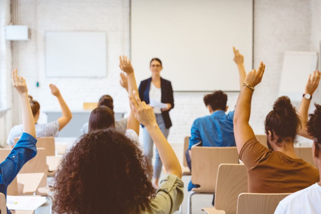 Image of male and female students raising hands in classroom.