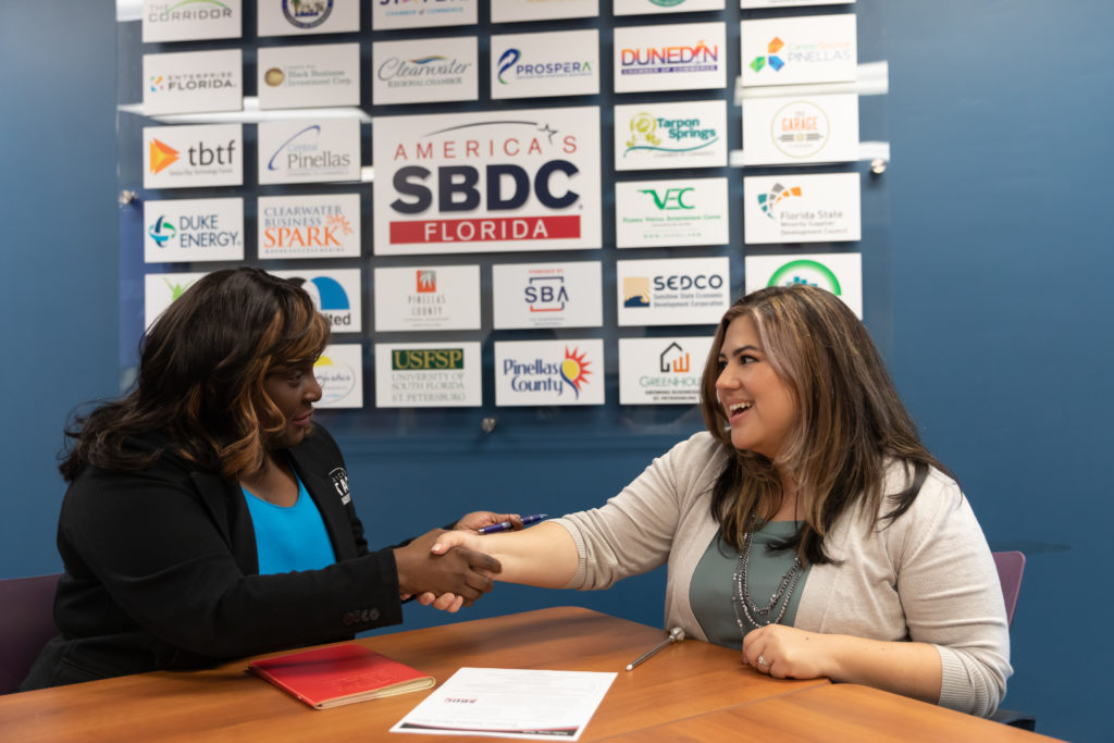 Yolanda Goodloe and Karisa Rojas-Norton, meeting at a table in front of SBDC signage.
