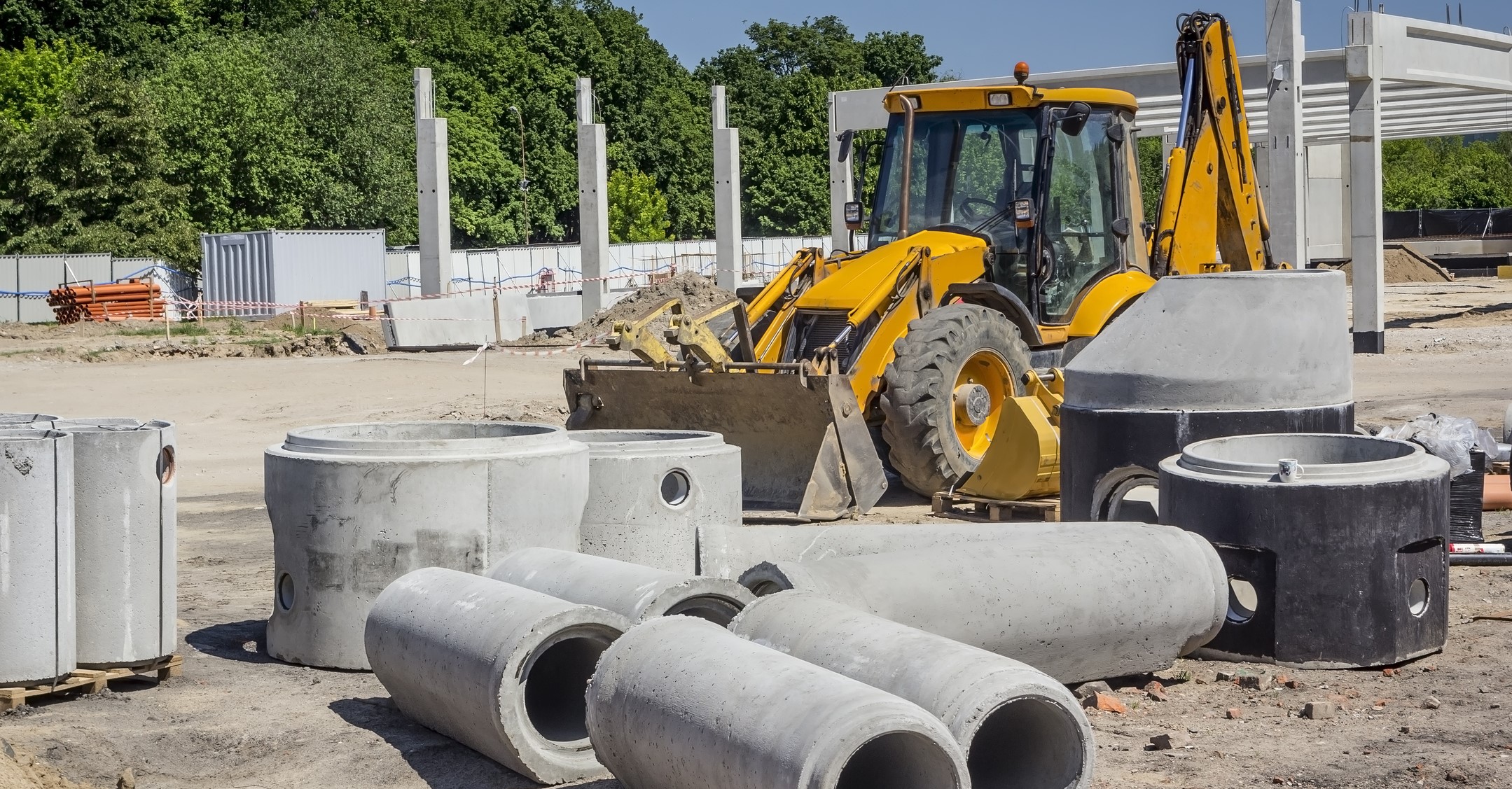 Concrete drainage pipes, earth mover and concrete warehouse in background